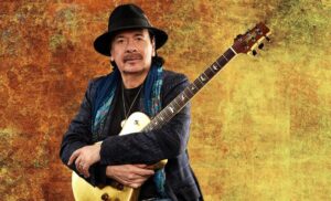 santana posing with a guitar and golden and orange wallpaper